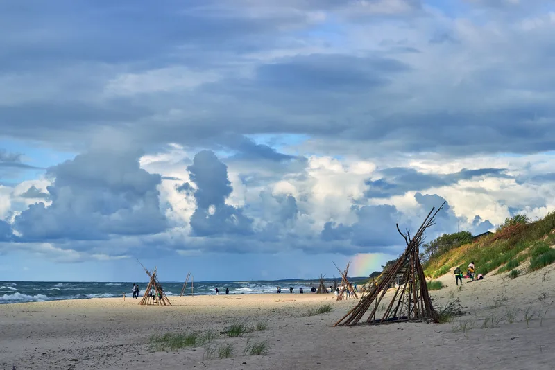 Beautiful Cloudy Sky With Rainbow Sandy Beach With Wigwams People Having Rest Sea