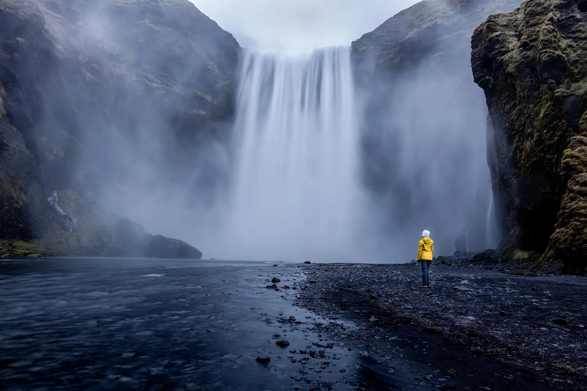 Person Wearing Yellow Jacket Standing Mesmerizing Waterfall. Nature wallpaper. 4000×2667px. Free download for personal use.