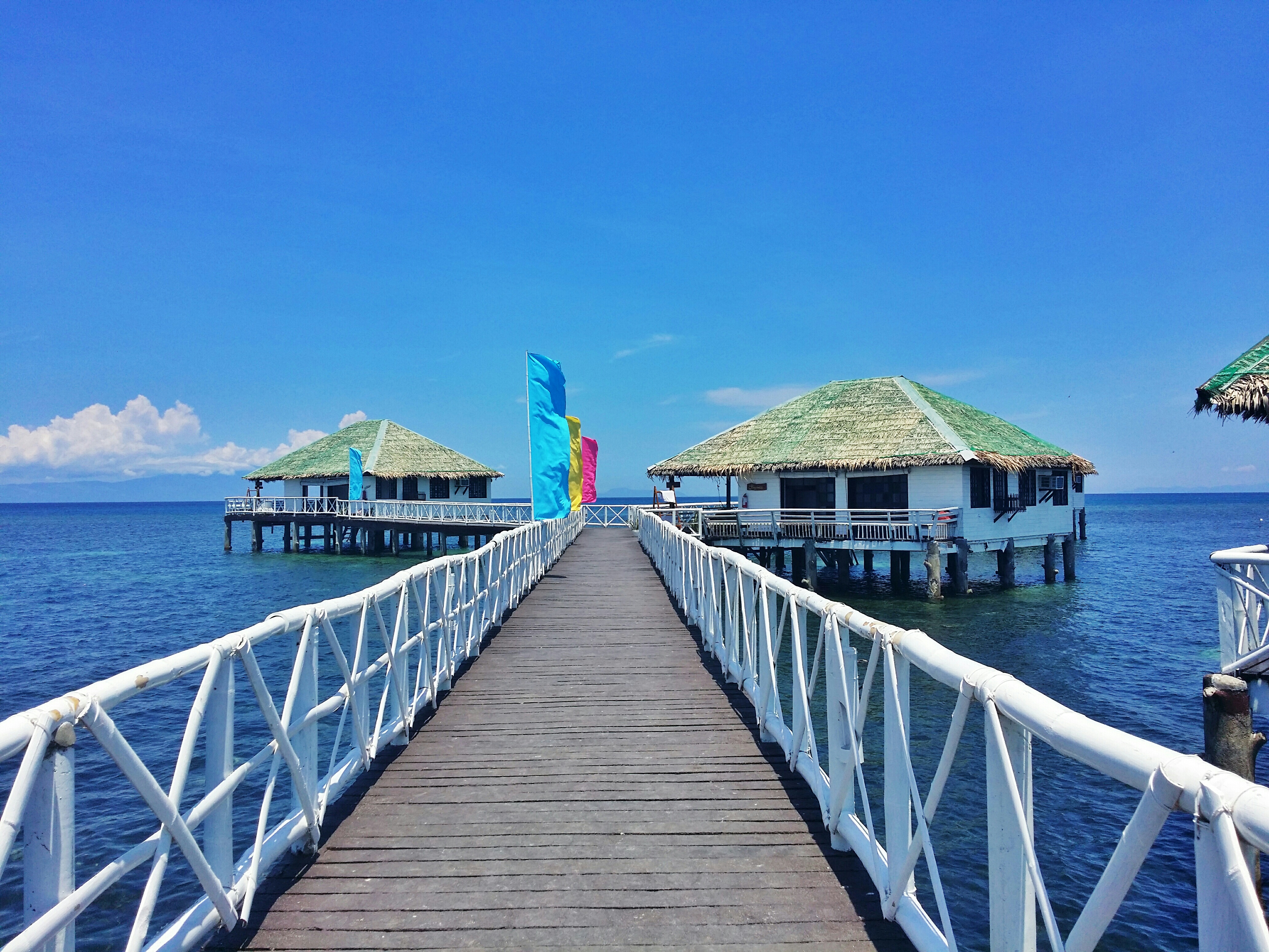 Pier Leading Towards Stilt Houses Sea Against Blue Sky