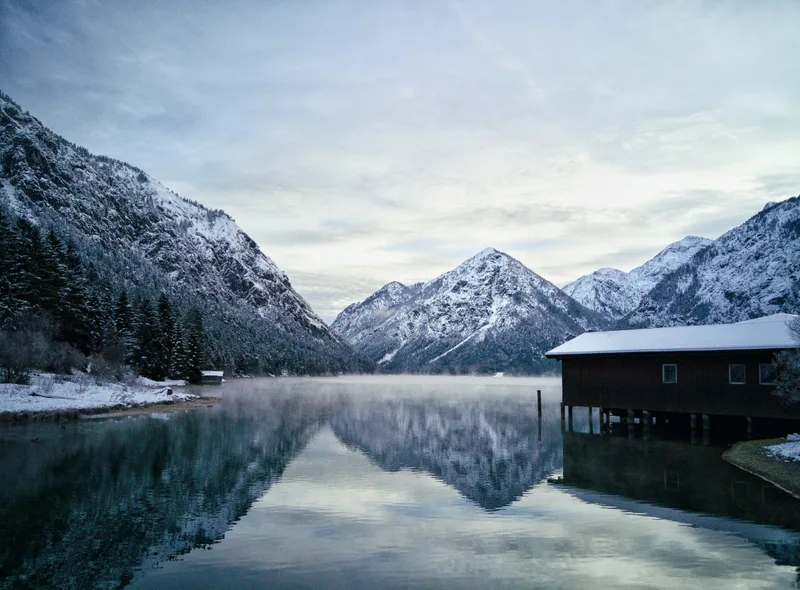 Residence House Near Lake Surrounded By Beautiful Rocky Mountains Covered With Snow